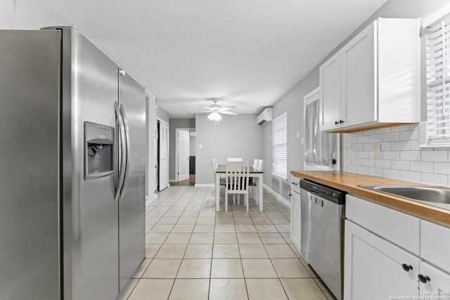 kitchen with appliances with stainless steel finishes, tasteful backsplash, a wall mounted air conditioner, white cabinets, and light tile patterned flooring