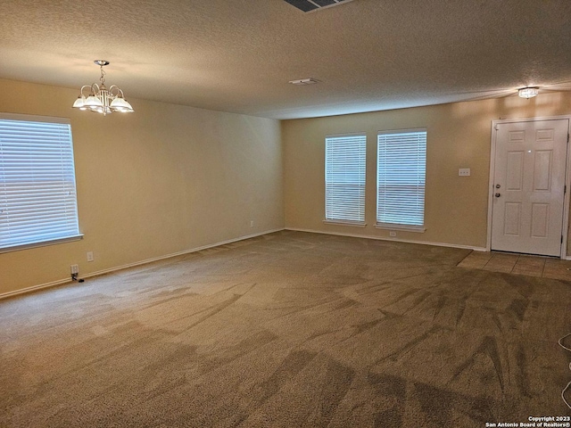 spare room featuring a chandelier, carpet, and a textured ceiling