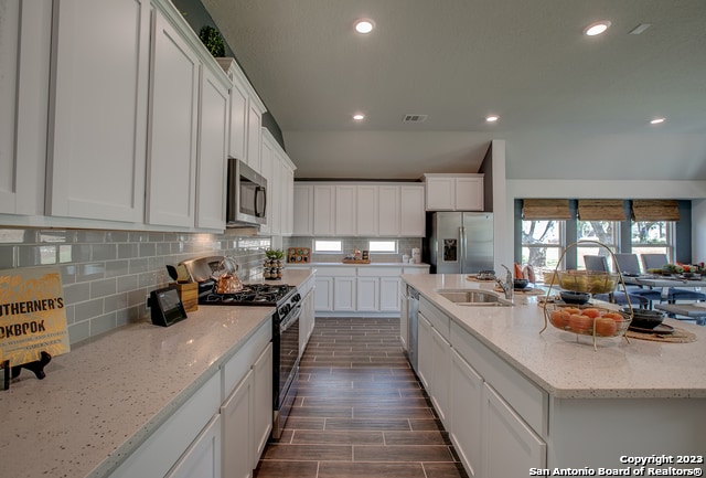 kitchen with white cabinetry, stainless steel appliances, light stone countertops, and a center island with sink