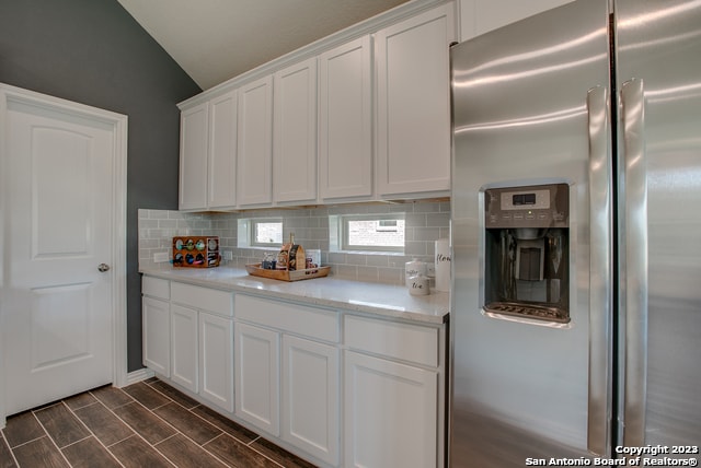 kitchen with stainless steel refrigerator with ice dispenser, lofted ceiling, light stone counters, tasteful backsplash, and white cabinets