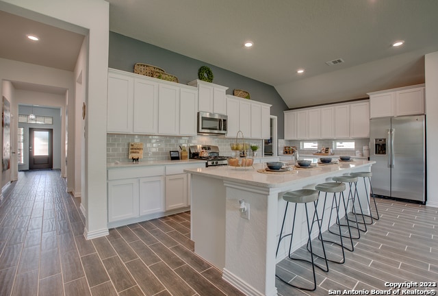 kitchen featuring stainless steel appliances, white cabinetry, a center island with sink, and backsplash