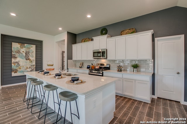 kitchen featuring white cabinetry, backsplash, stainless steel appliances, and a center island with sink