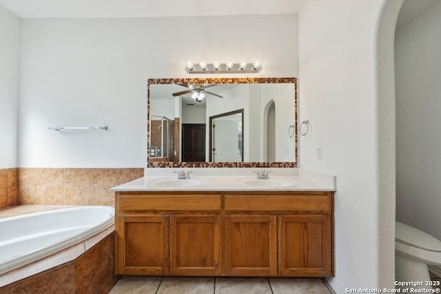 bathroom featuring ceiling fan, a relaxing tiled tub, vanity, tile patterned floors, and toilet