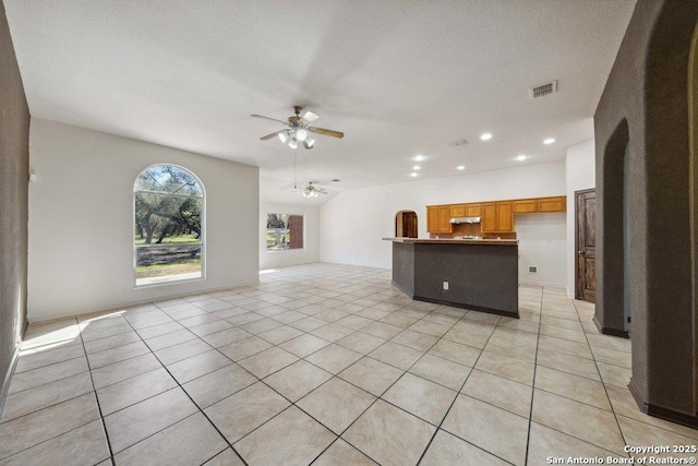 unfurnished living room with ceiling fan, vaulted ceiling, a textured ceiling, and light tile patterned floors