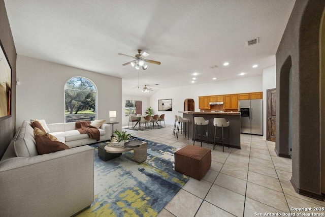 tiled living room with lofted ceiling, a textured ceiling, and ceiling fan