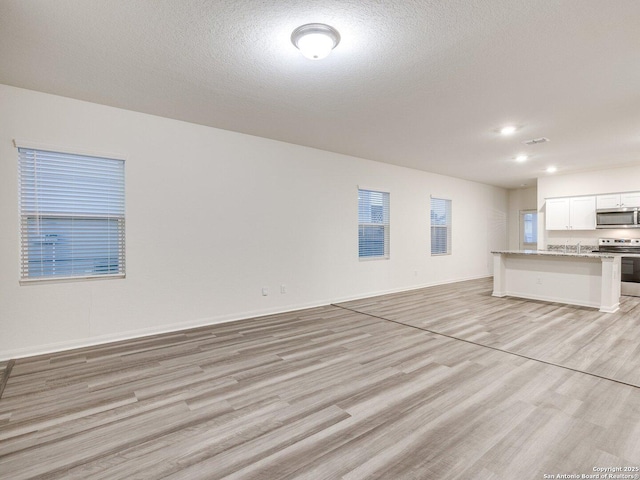 unfurnished living room with sink, a textured ceiling, and light wood-type flooring