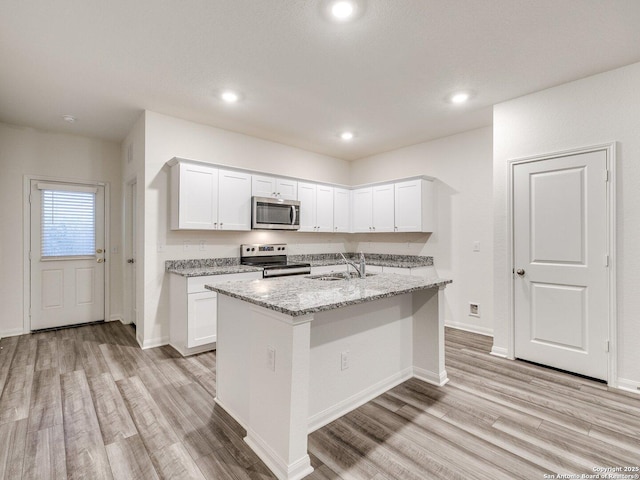 kitchen with sink, white cabinets, a kitchen island with sink, light stone counters, and stainless steel appliances