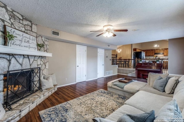 living room with dark hardwood / wood-style floors, ceiling fan, a stone fireplace, and a textured ceiling