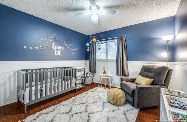 bedroom featuring ceiling fan, dark wood-type flooring, a nursery area, and a textured ceiling