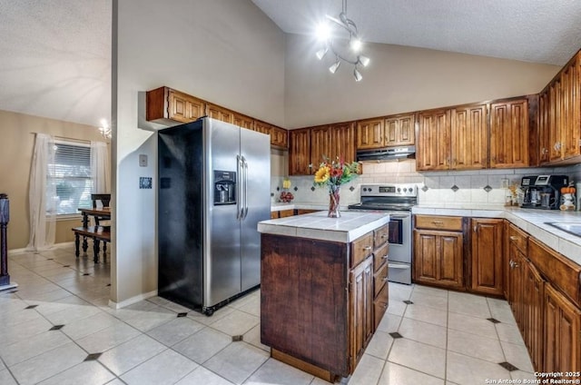 kitchen featuring a kitchen island, appliances with stainless steel finishes, lofted ceiling, tile counters, and light tile patterned floors