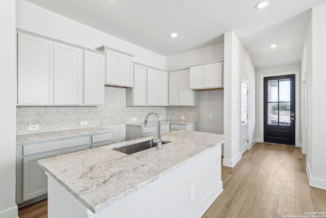 14603 Rainwater Trl, San Antonio, TX 78253 - kitchen featuring light wood-style flooring, light stone countertops, a kitchen island with sink, a sink, and backsplash