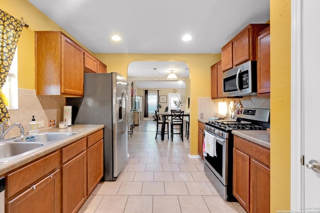 kitchen with appliances with stainless steel finishes, sink, light tile patterned floors, and decorative backsplash