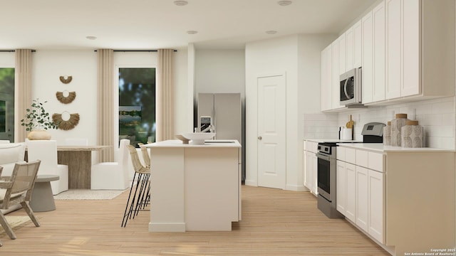 kitchen featuring appliances with stainless steel finishes, a center island with sink, light hardwood / wood-style floors, white cabinets, and a kitchen bar