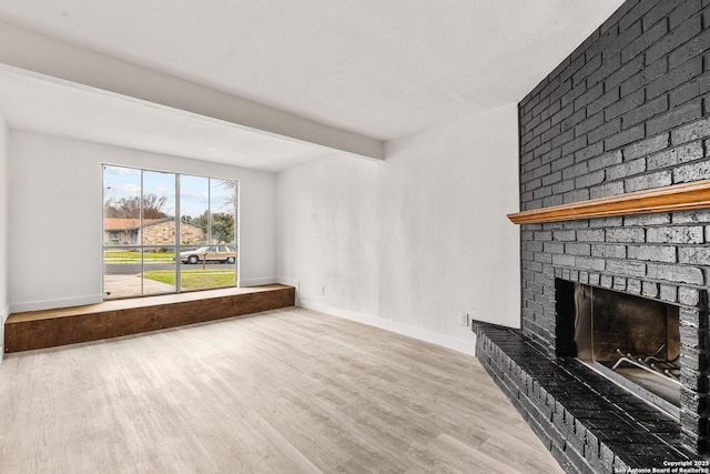 unfurnished living room with beam ceiling, a brick fireplace, and light hardwood / wood-style floors