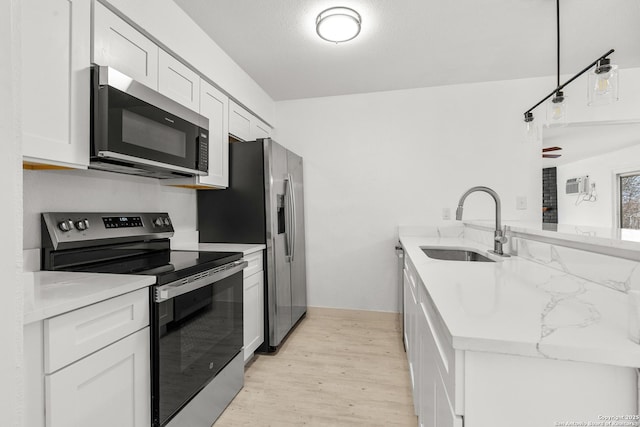 kitchen with stainless steel appliances, light stone countertops, sink, and white cabinets