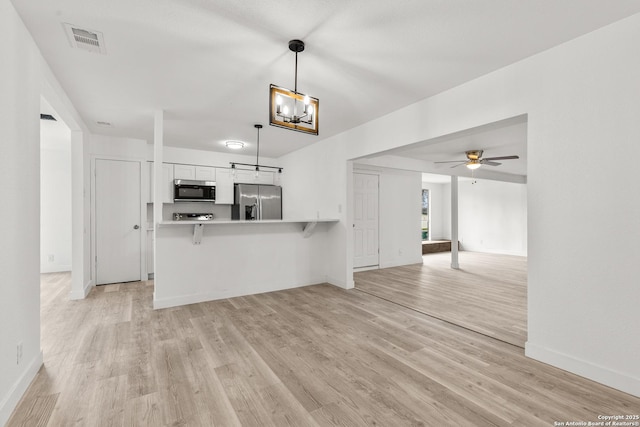 interior space featuring pendant lighting, a breakfast bar area, white cabinets, stainless steel fridge, and kitchen peninsula