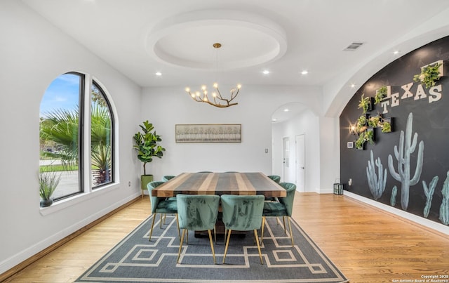 dining room featuring a notable chandelier, light hardwood / wood-style floors, and a tray ceiling