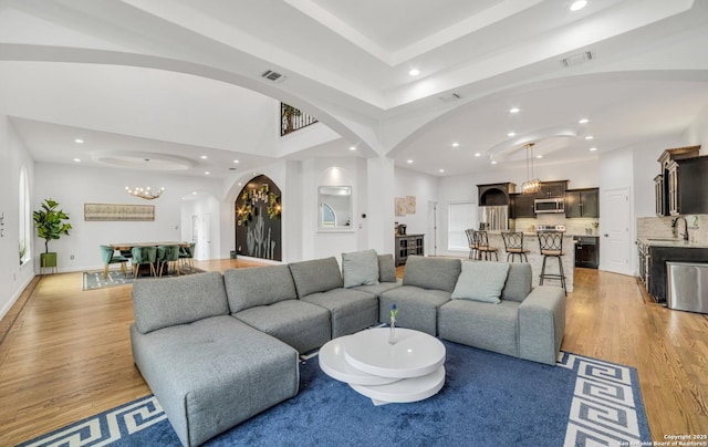 living room featuring sink, light hardwood / wood-style flooring, and a notable chandelier