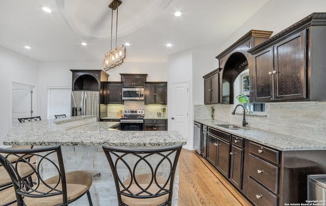 kitchen featuring sink, dark brown cabinets, hanging light fixtures, light wood-type flooring, and stainless steel appliances