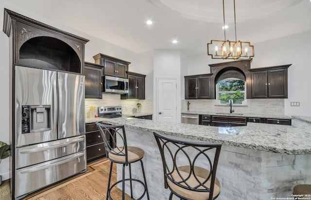 kitchen with sink, decorative light fixtures, light hardwood / wood-style flooring, stainless steel appliances, and light stone countertops