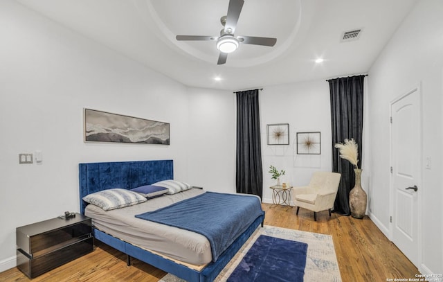 bedroom with ceiling fan, wood-type flooring, and a raised ceiling