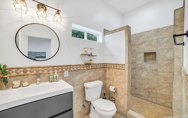 bathroom with tiled shower, vanity, toilet, and tile walls