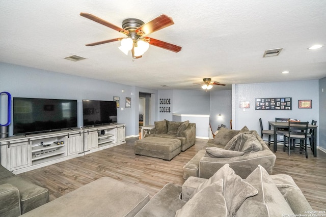 living room featuring ceiling fan, a textured ceiling, and light wood-type flooring