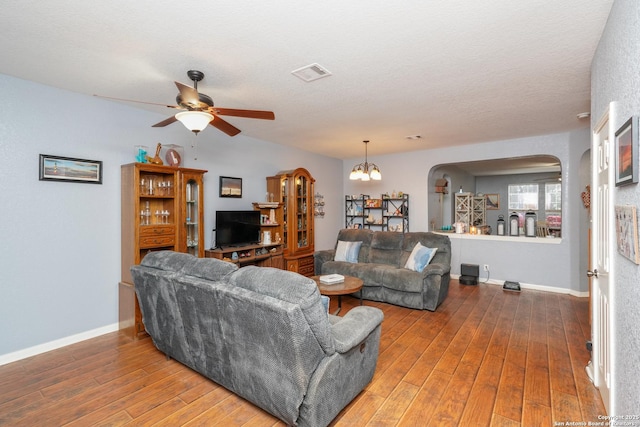 living room with wood-type flooring, ceiling fan with notable chandelier, and a textured ceiling