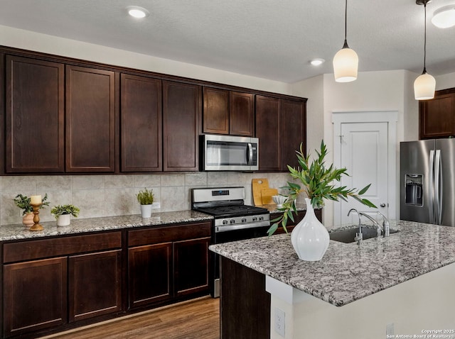 kitchen with pendant lighting, stainless steel appliances, light stone countertops, and sink