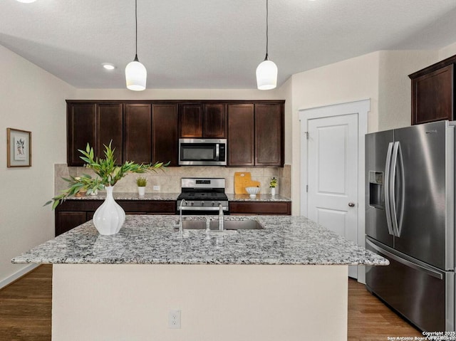 kitchen with a kitchen island with sink, hanging light fixtures, light stone counters, and stainless steel appliances