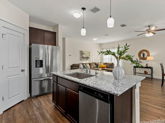 kitchen with dark brown cabinetry, sink, decorative light fixtures, stainless steel appliances, and a kitchen island with sink