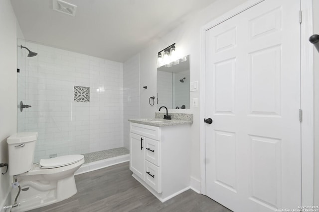 bathroom with vanity, toilet, hardwood / wood-style floors, and a tile shower