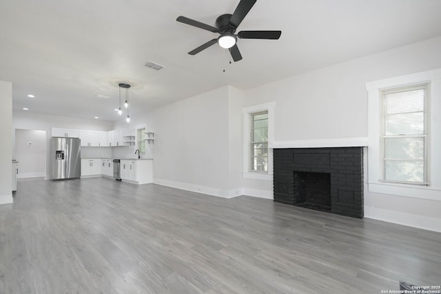 unfurnished living room featuring ceiling fan, sink, a fireplace, and hardwood / wood-style floors