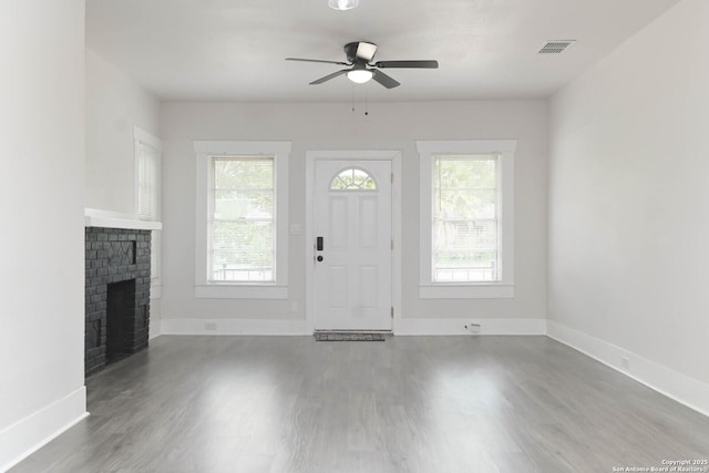 unfurnished living room featuring hardwood / wood-style flooring, a brick fireplace, and a healthy amount of sunlight