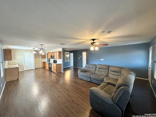 living room featuring ceiling fan with notable chandelier, dark hardwood / wood-style floors, and sink