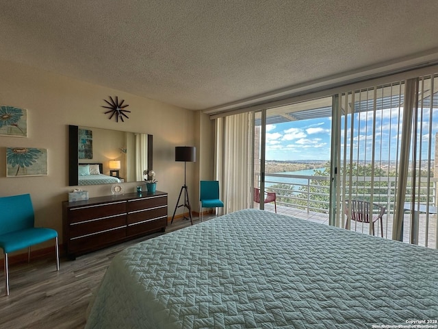 bedroom with a water view, wood-type flooring, access to exterior, and a textured ceiling