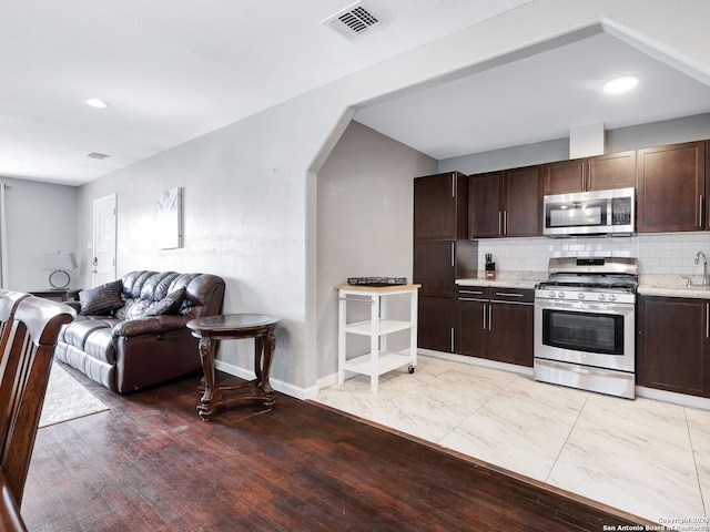 kitchen featuring stainless steel appliances, visible vents, open floor plan, light countertops, and decorative backsplash