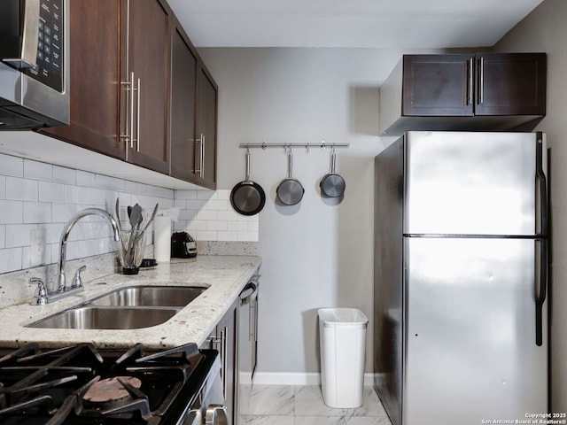 kitchen featuring stainless steel appliances, light stone counters, a sink, and dark brown cabinets