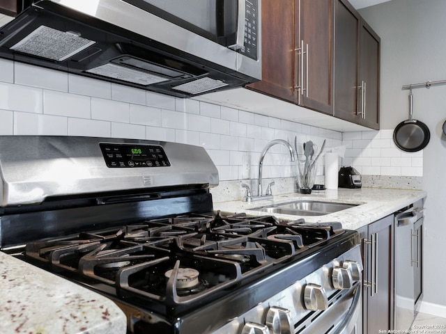 kitchen featuring light stone counters, decorative backsplash, appliances with stainless steel finishes, a sink, and dark brown cabinetry