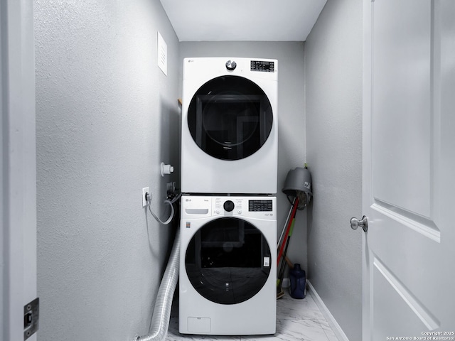 laundry area with a textured wall, laundry area, baseboards, marble finish floor, and stacked washing maching and dryer