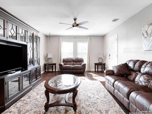 living room with dark wood-style flooring, visible vents, ceiling fan, and baseboards