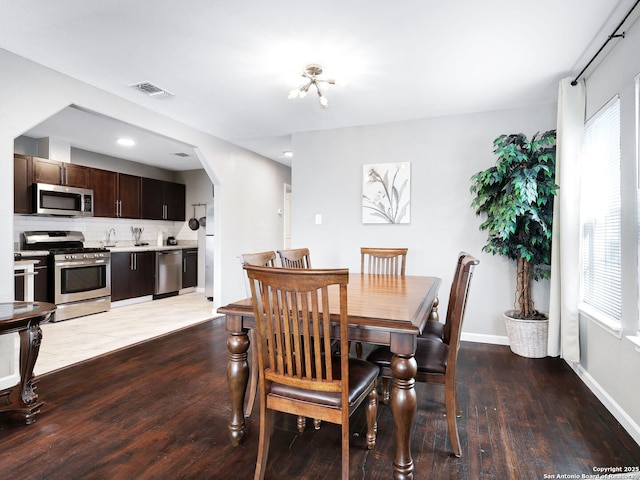 dining room featuring arched walkways, wood finished floors, visible vents, and baseboards