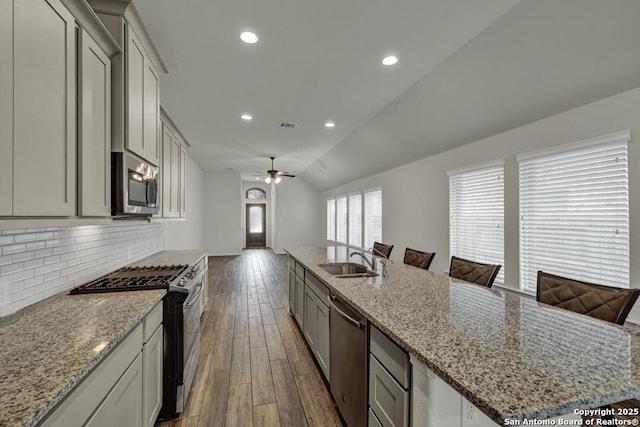 kitchen with sink, vaulted ceiling, an island with sink, stainless steel appliances, and backsplash