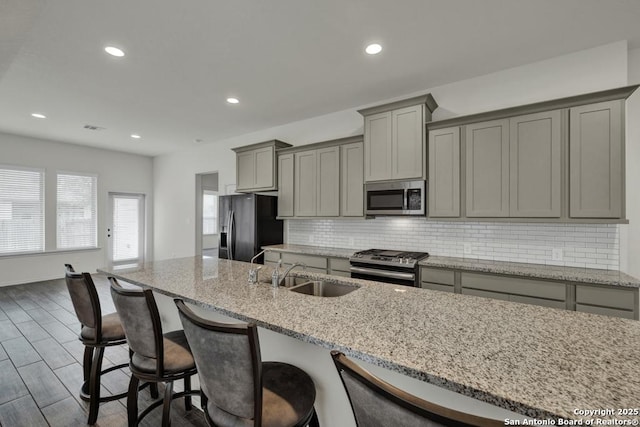 kitchen featuring sink, gray cabinetry, stainless steel appliances, light stone counters, and decorative backsplash