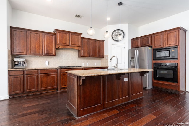 kitchen featuring an island with sink, sink, hanging light fixtures, light stone counters, and black appliances