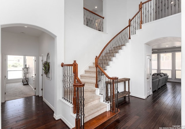 staircase featuring wood-type flooring, a healthy amount of sunlight, and a high ceiling