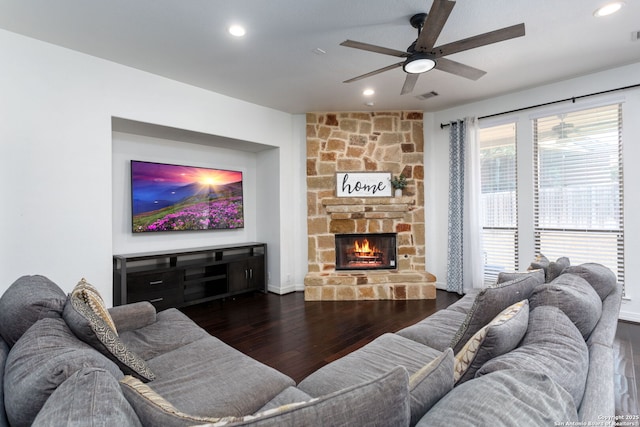 living room with a stone fireplace, dark wood-type flooring, and ceiling fan