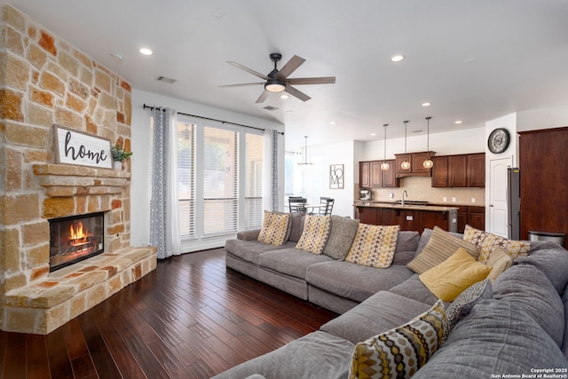 living room featuring dark wood-type flooring, ceiling fan, a fireplace, and sink