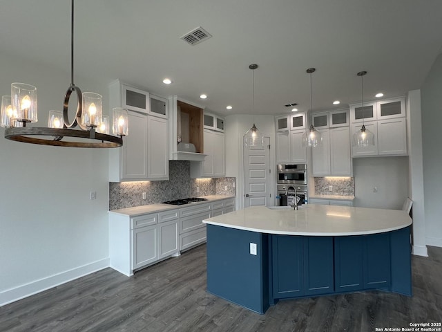 kitchen featuring double oven, gas cooktop, visible vents, white cabinets, and a center island with sink