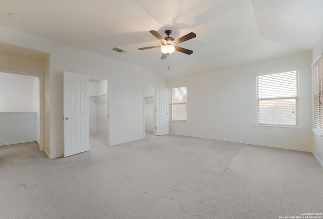 unfurnished bedroom with ceiling fan, a walk in closet, lofted ceiling, and light carpet